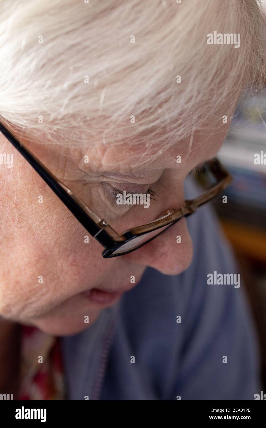 An old women with glasses looking down and reading with selective focus on the eye Stock Photo