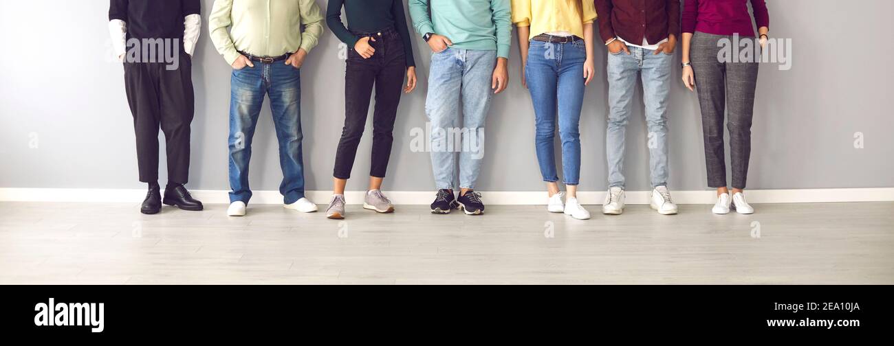 Cropped image of the legs of people in ordinary clothes and shoes standing in a row near the wall. Stock Photo
