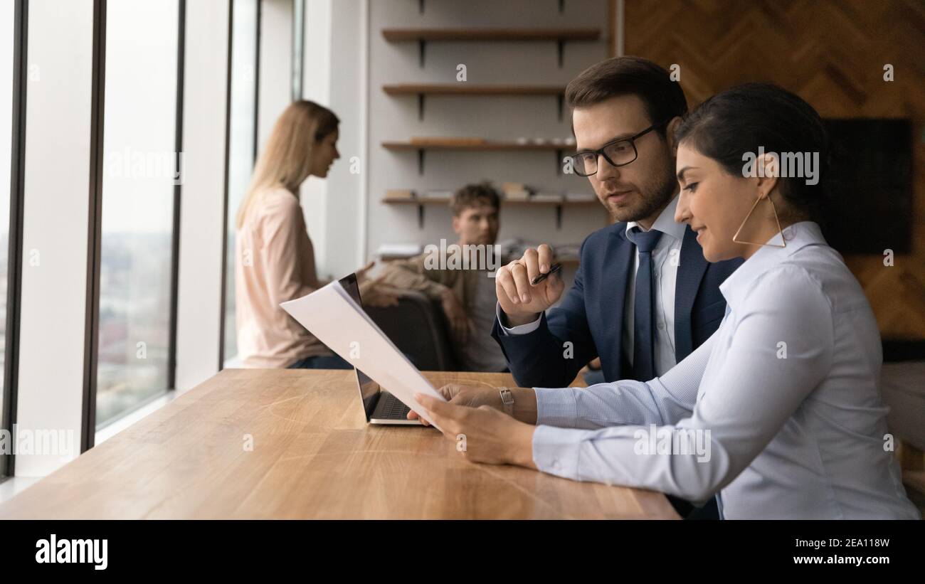 Two diverse teammates mentor intern discuss documents at coworking area Stock Photo