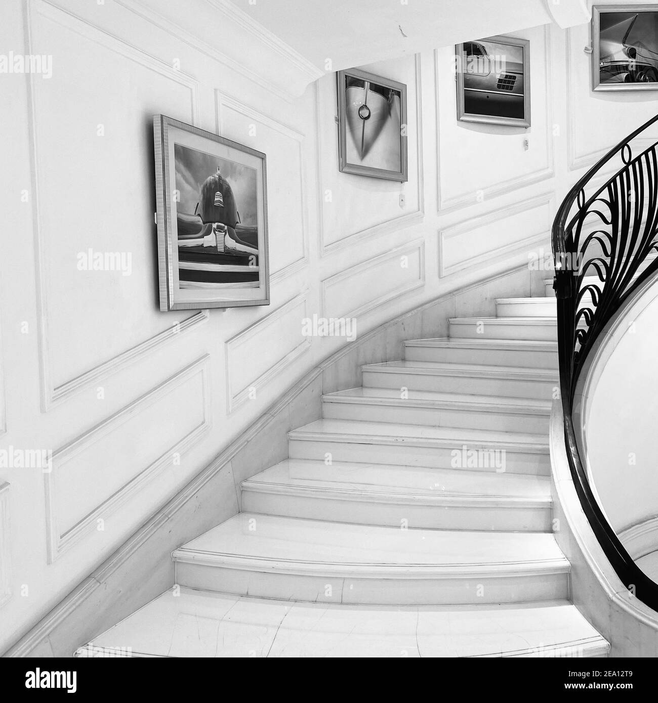 Black and white interior design of hallway. Staircase with marble stairs and forged handrails. Pictures of some random car parts on the wall Stock Photo