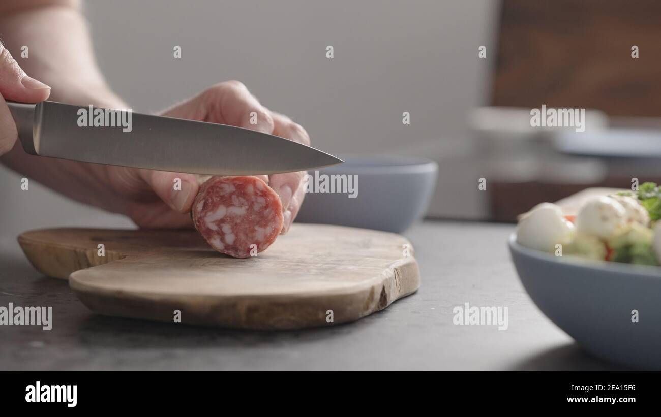man slicing salame on olive wood board on concrete countertop, wide photo Stock Photo