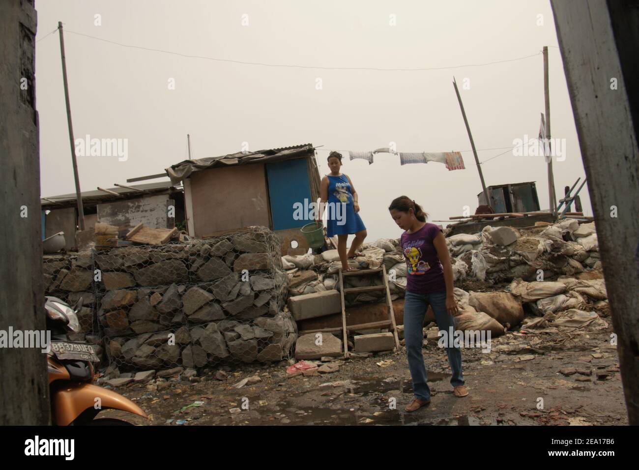 Women stepping out of their house in Muara Baru area, in the coastal area of Jakarta, Indonesia. Several houses in the area were built above sea water on stilts, just outside the coastal protection structure connecting the community with a coastal road and their land-based neighbours. Muara Baru, Penjaringan, North Jakarta, Jakarta, Indonesia. Archival photo. Stock Photo