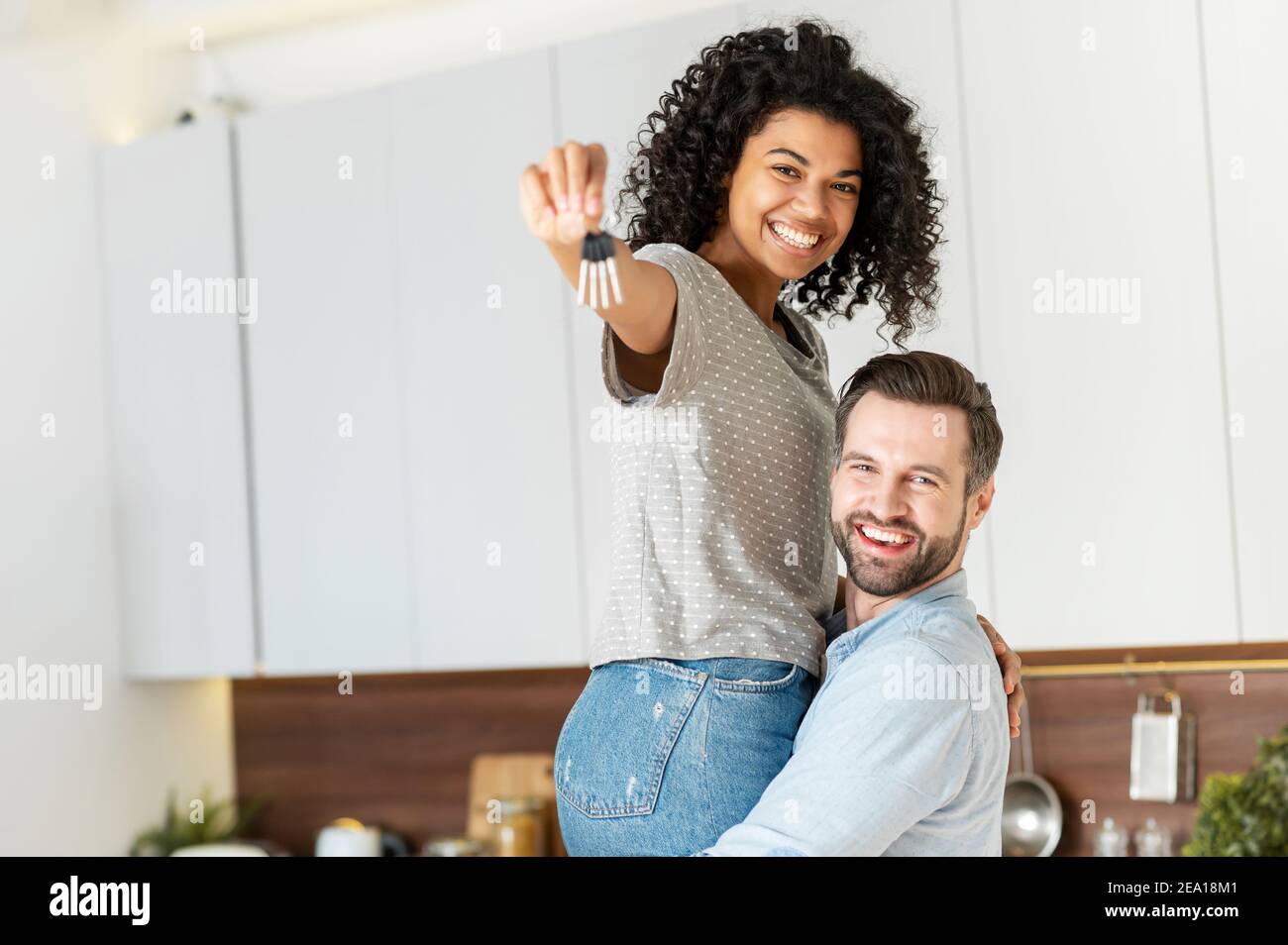 Dreams came true. Excited multiracial couple buying a property, got a mortgage apartment. A guy is carrying his beautiful girlfriend on the arms with Stock Photo