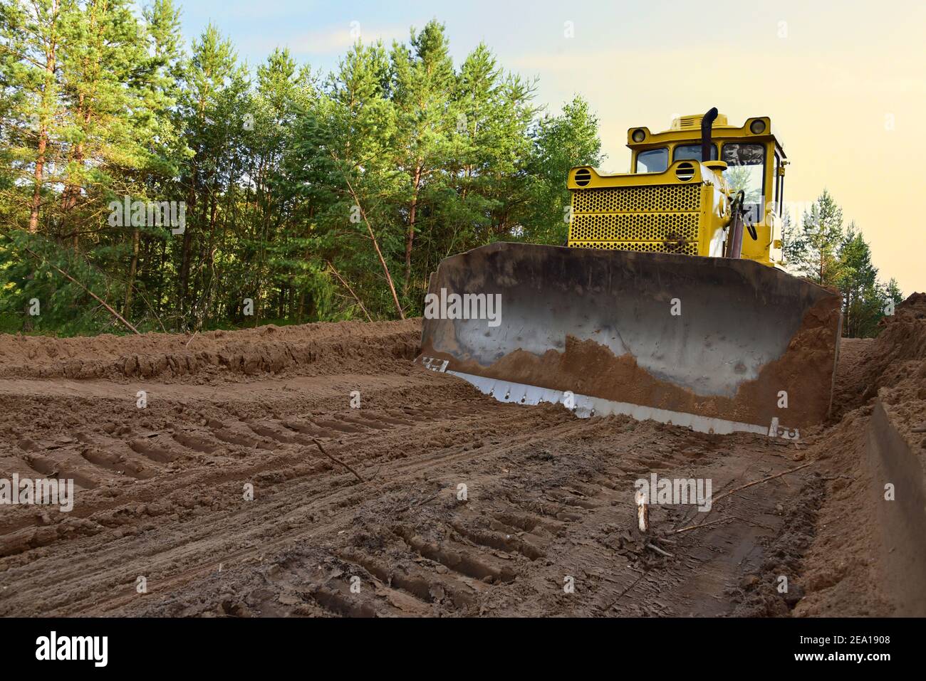 Dozer during clearing forest for construction new road . Yellow Bulldozer at forestry work Earth-moving equipment at road work, land clearing, grading Stock Photo