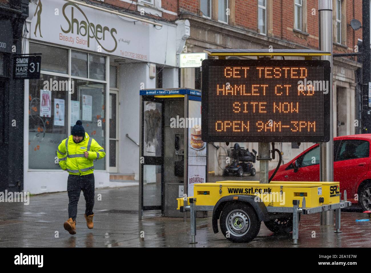 Westcliff on Sea, Essex, UK. 7th Feb, 2021. Storm Darcy reached the area later than initially forecast, with the area remaining wet overnight. Snow and sleety flurries arrived from around 7am. A male in construction site style clothing running towards railway station. COVID 19 lockdown warnings remain in place. Matrix sign asking people to get tested in local test site at Hamlet Court Road Stock Photo