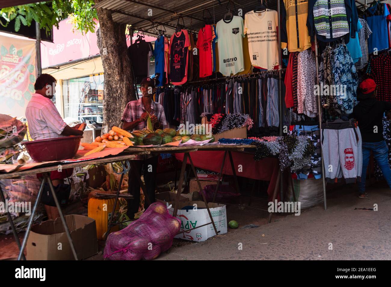 Vendor in a shop at a bazaar in Sri Lanka sellin clothing and vegetables Stock Photo