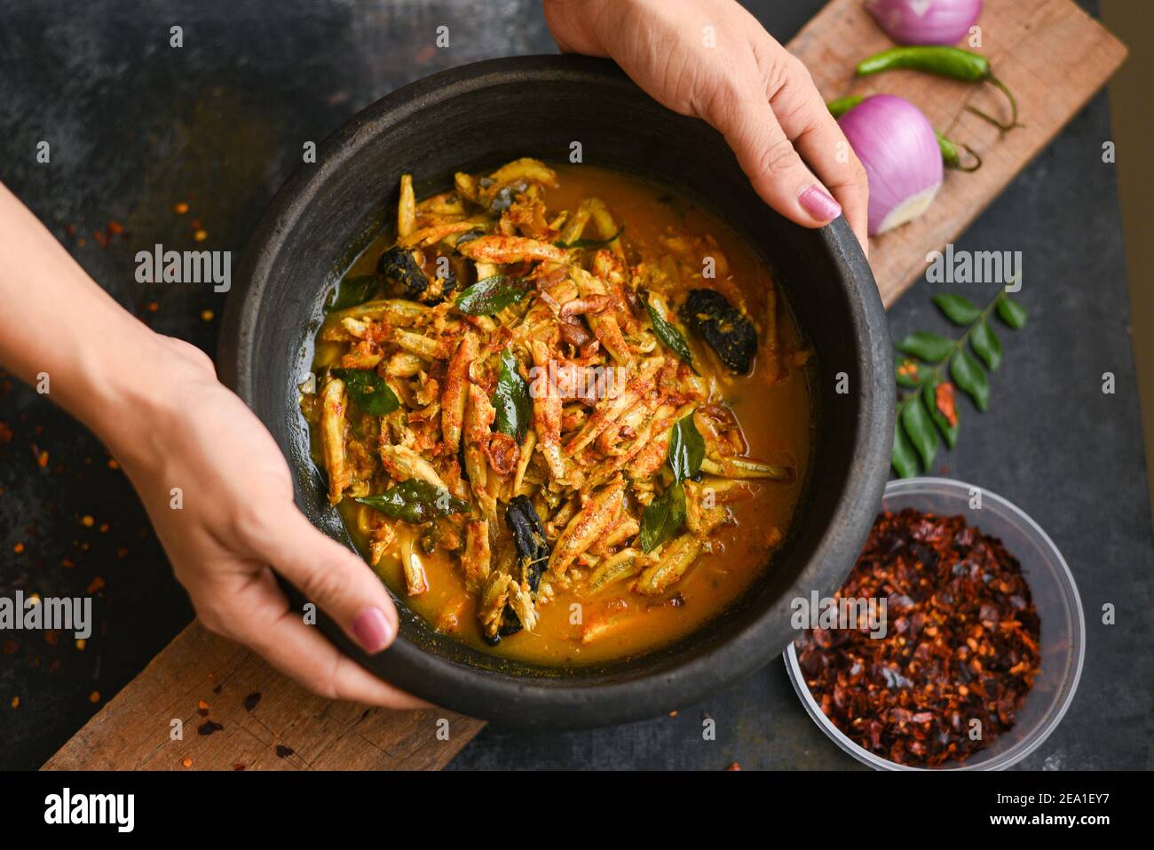 Top view spicy hot anchovy Kerala fish curry. Indian food. Woman hand