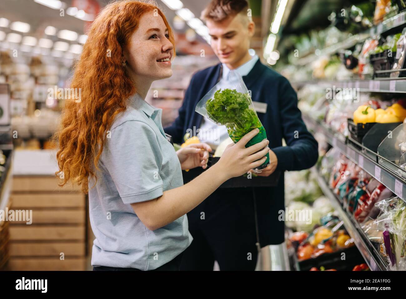 Male and female workers packing fresh produce on the shelves in supermarket. Grocery store