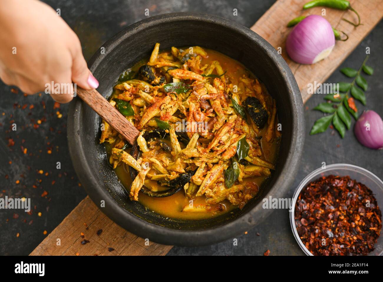 Top view spicy hot anchovy Kerala fish curry. Indian food. Woman hand