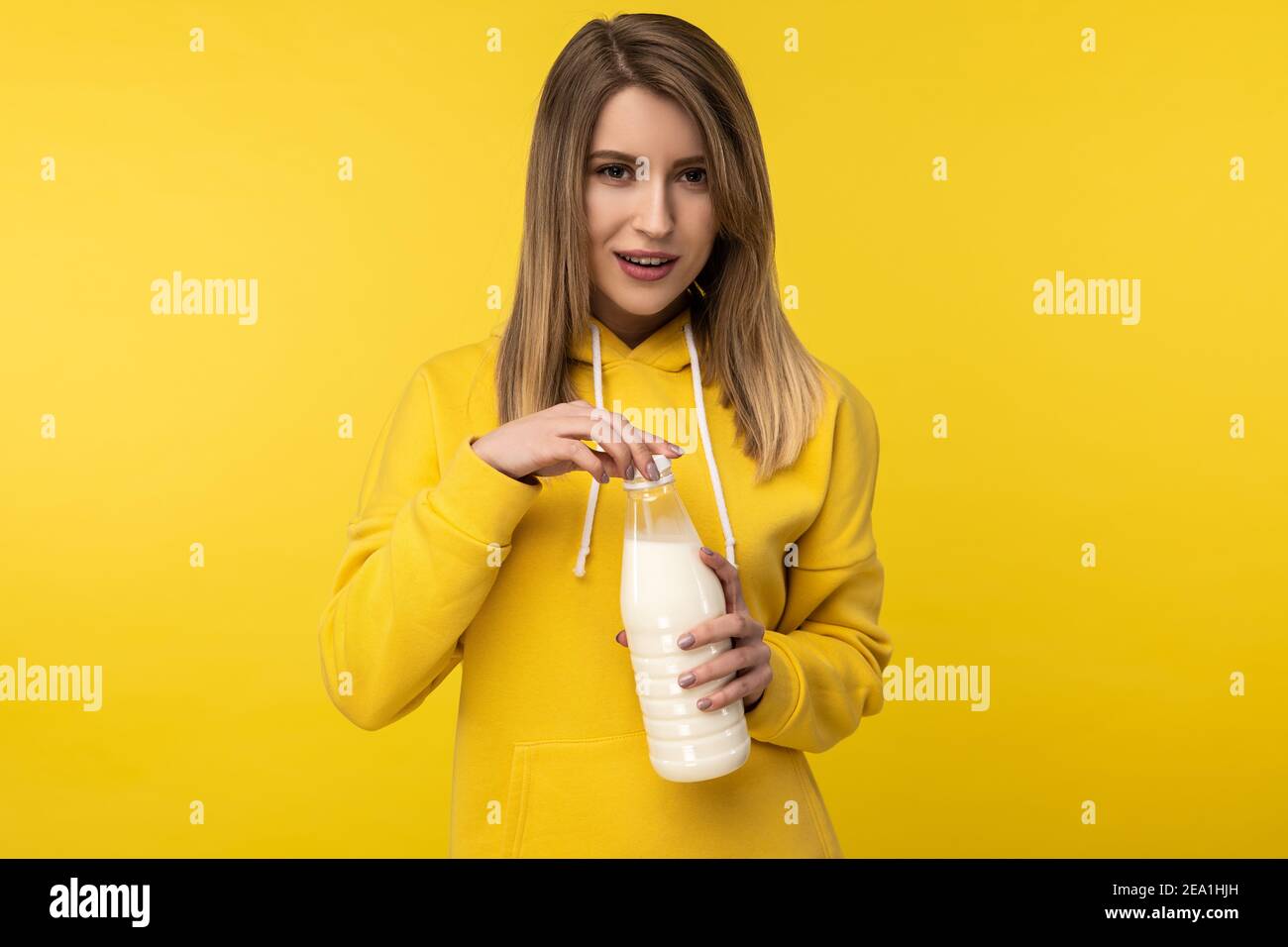 Photo of attractive lady holds bootle of milk, feels nice about dairy products. Wears casual yellow hoody, isolated yellow color background Stock Photo