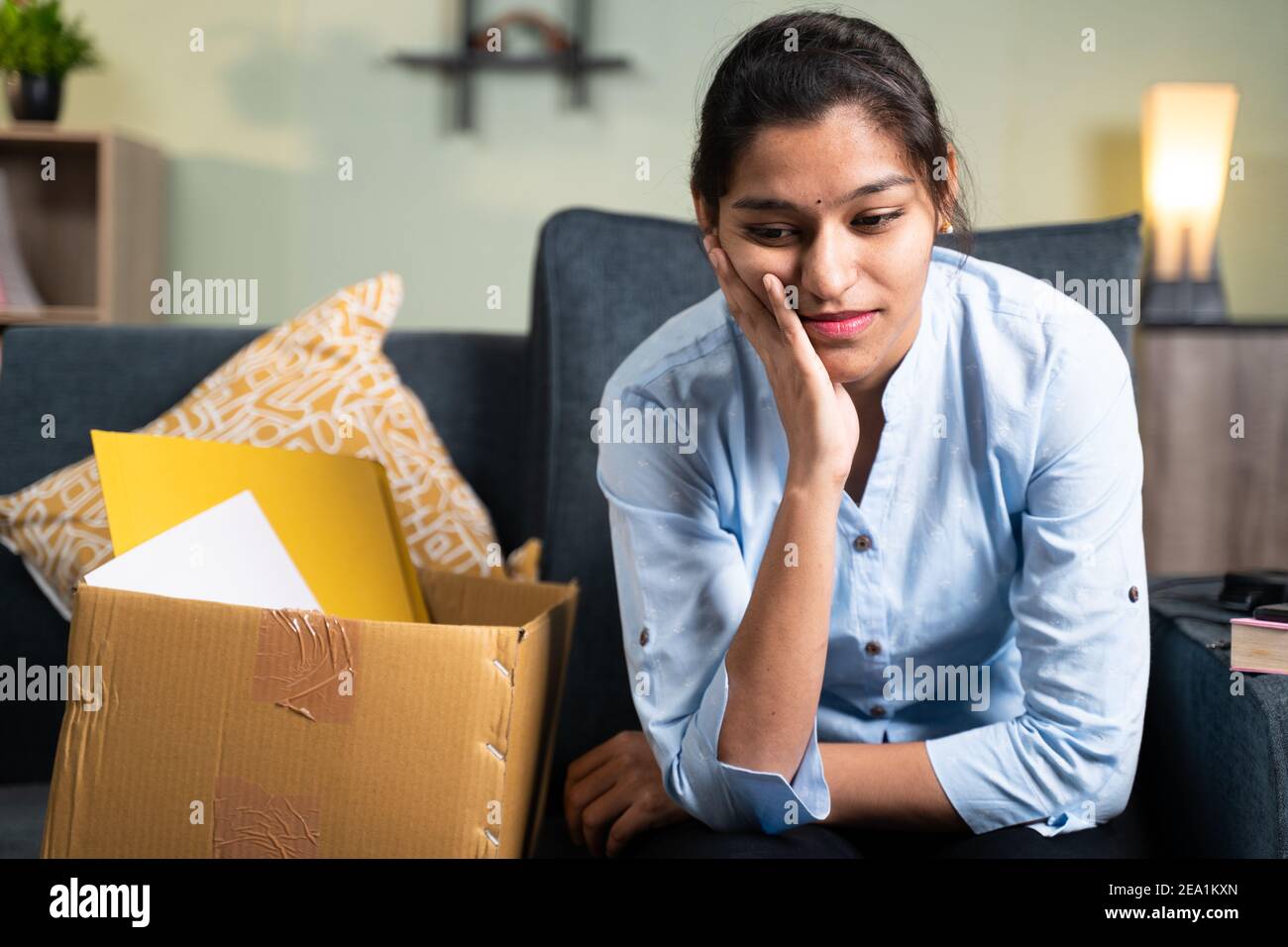 Worried young business woman sitting sadly on sofa at home due to loss of job, employment or fired from the work Stock Photo