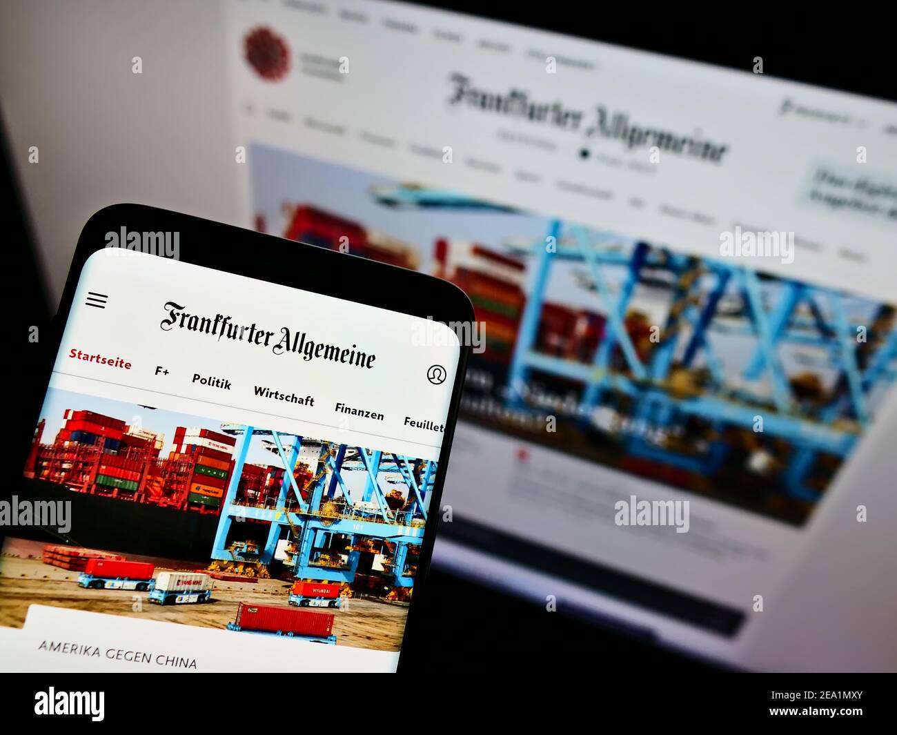 Mobile phone with website and logo of German newspaper Frankfurter Allgemeine Zeitung (FAZ) on screen in front of monitor. Focus on phone display. Stock Photo