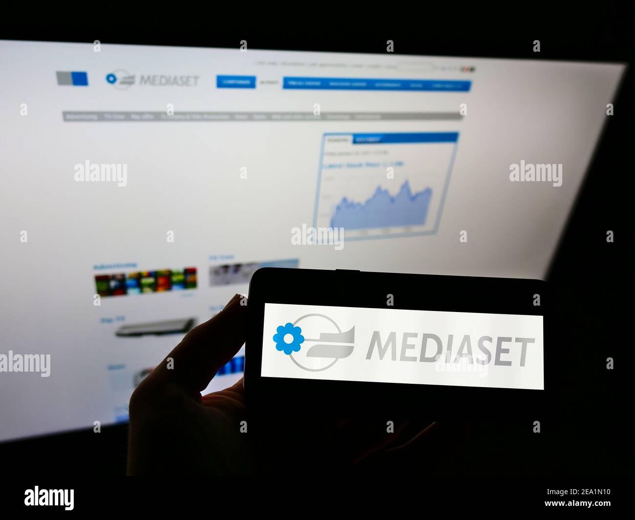 Person holding smartphone with business logo of Italian mass media company Mediaset S.p.A. on screen in front of website. Focus on phone display. Stock Photo