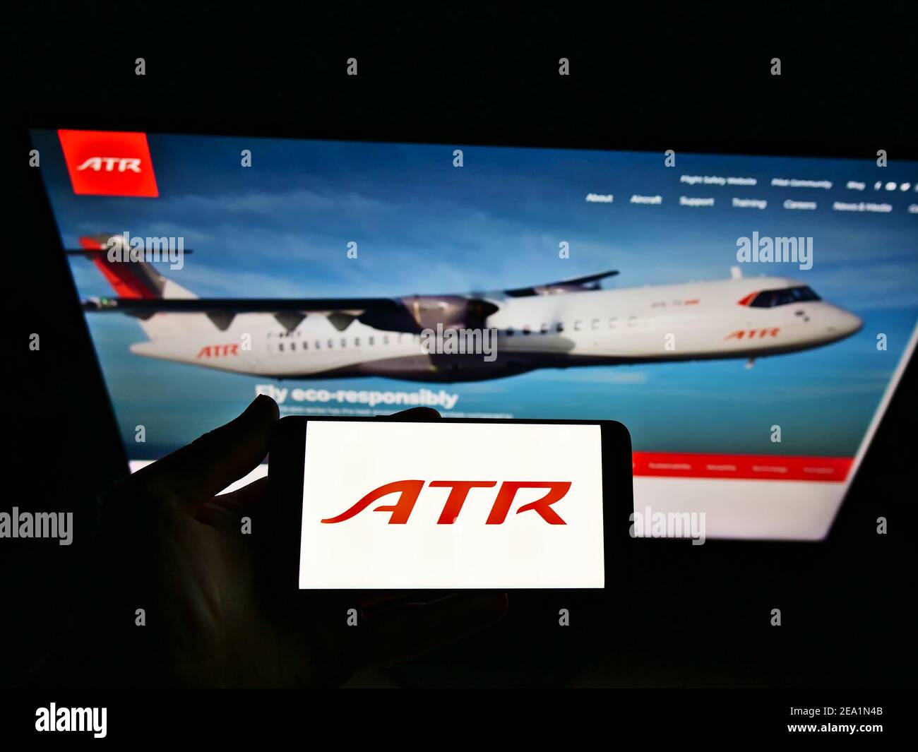 Person holding smartphone with logo of aircraft manufacturer Avions de Transport Régional (ATR) on screen in front of website. Focus on phone display. Stock Photo