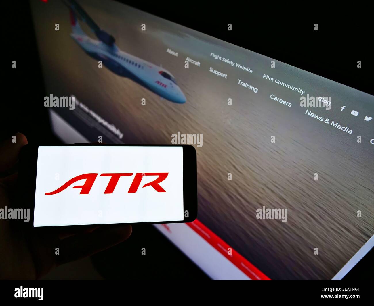 Person holding mobile phone with logo of aircraft manufacturer Avions de Transport Régional (ATR) on screen with web page. Focus on cellphone display. Stock Photo