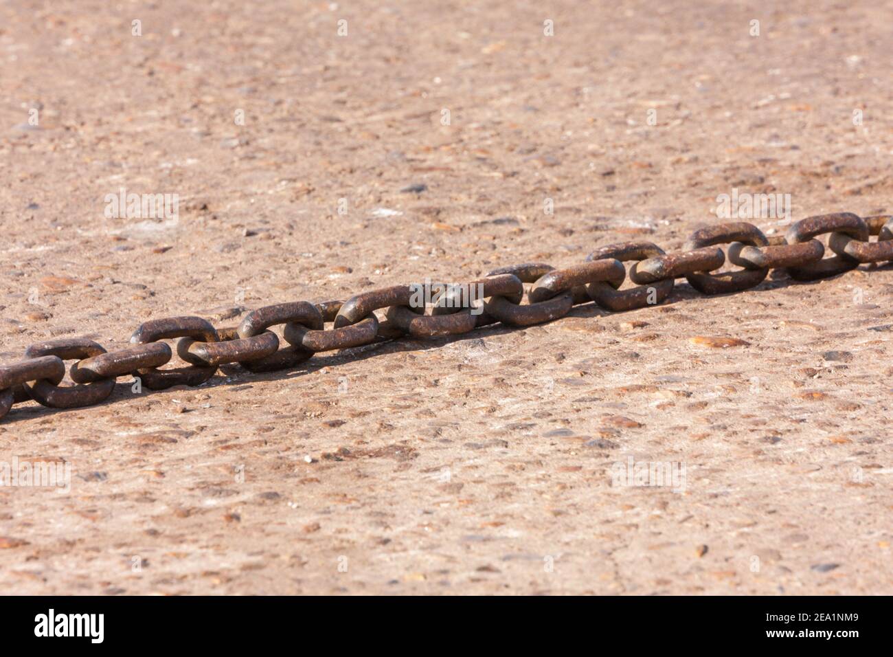 Rusty iron ship chain laying on a concrete quayside.  UK Stock Photo