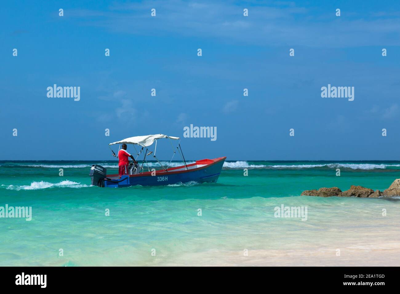 Barbadian men in red skirt  on blue boat in azure water of Caribbean sea. Worthing beach in Barbados. Stock Photo