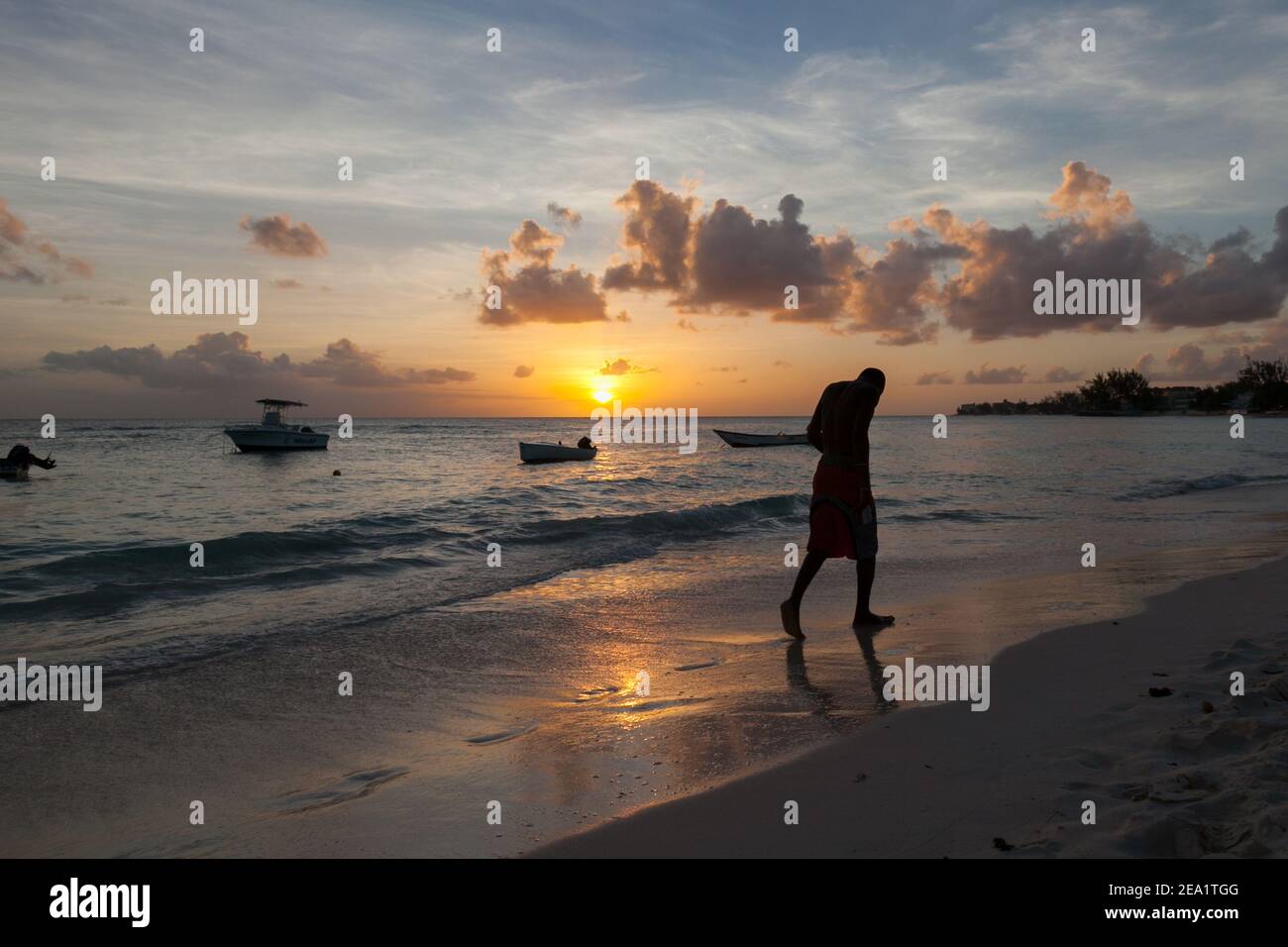 Young  men running along beach at sunset. Beautiful Worthing beach in Barbados Stock Photo