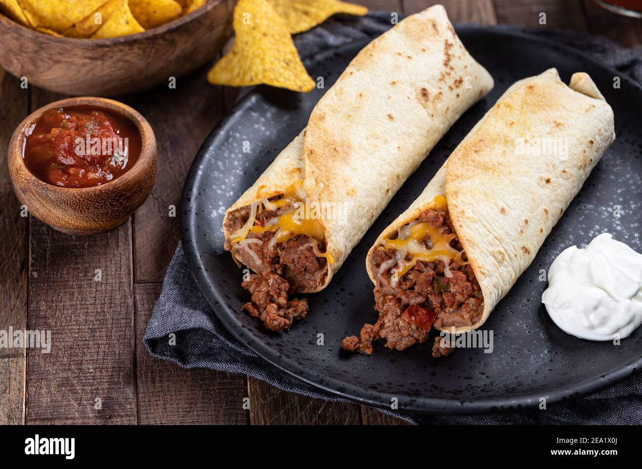Burritos with ground beef, refried beans and cheese on a black plate with salsa and tortilla