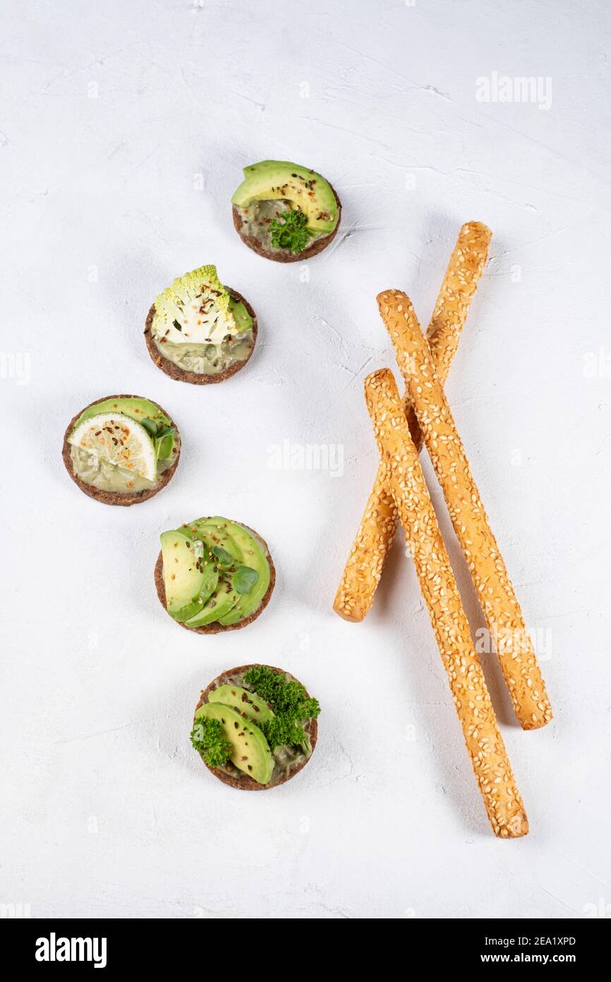 Whole wheat bread topped with avocado variants on white background with sesame sticks, text free space Stock Photo