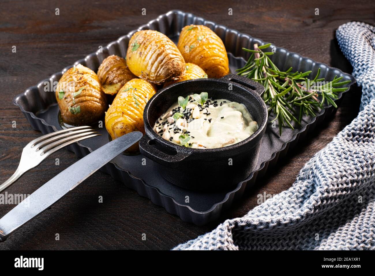 Baked pan baked potatoes (baked potatoes) in a black cast iron round skillet with garlic and olive oil, served with an avocado dip Stock Photo