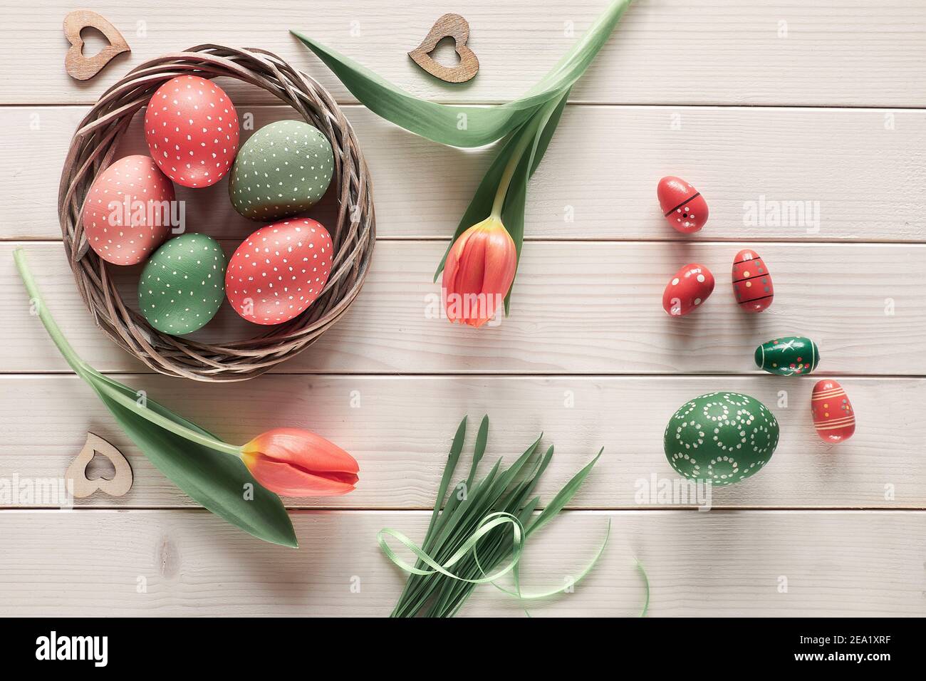 Flat lay with red tulips in rattan wreath basket and green grass. Decorative painted Easter eggs. Springtime, Easter background on rustic off white Stock Photo