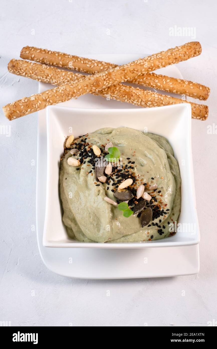 Avocado dip with sunflower seeds and pumpkin seeds, served in a white porcelain dish on a white background, with sesame sticks Stock Photo