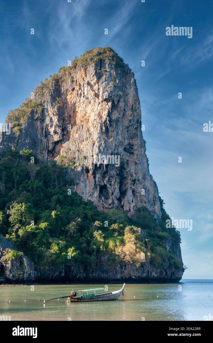 Giant rock formation stretches out into the sea at Railay Beach, near Krabi, Thailand, with Long-Tail boat on the sea in the foreground Stock Photo