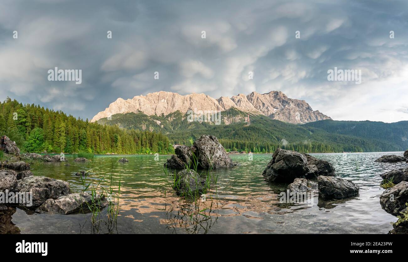 Rocks on the shore, Lake Eibsee lake in front of Zugspitze massif with Zugspitze, dramatic Mammaten clouds, Wetterstein range, near Grainau, Upper Stock Photo