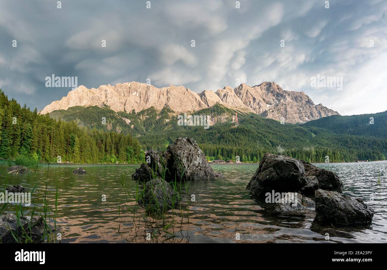 Rocks on the shore, Lake Eibsee lake in front of Zugspitze massif with Zugspitze, dramatic Mammaten clouds, Wetterstein range, near Grainau, Upper Stock Photo