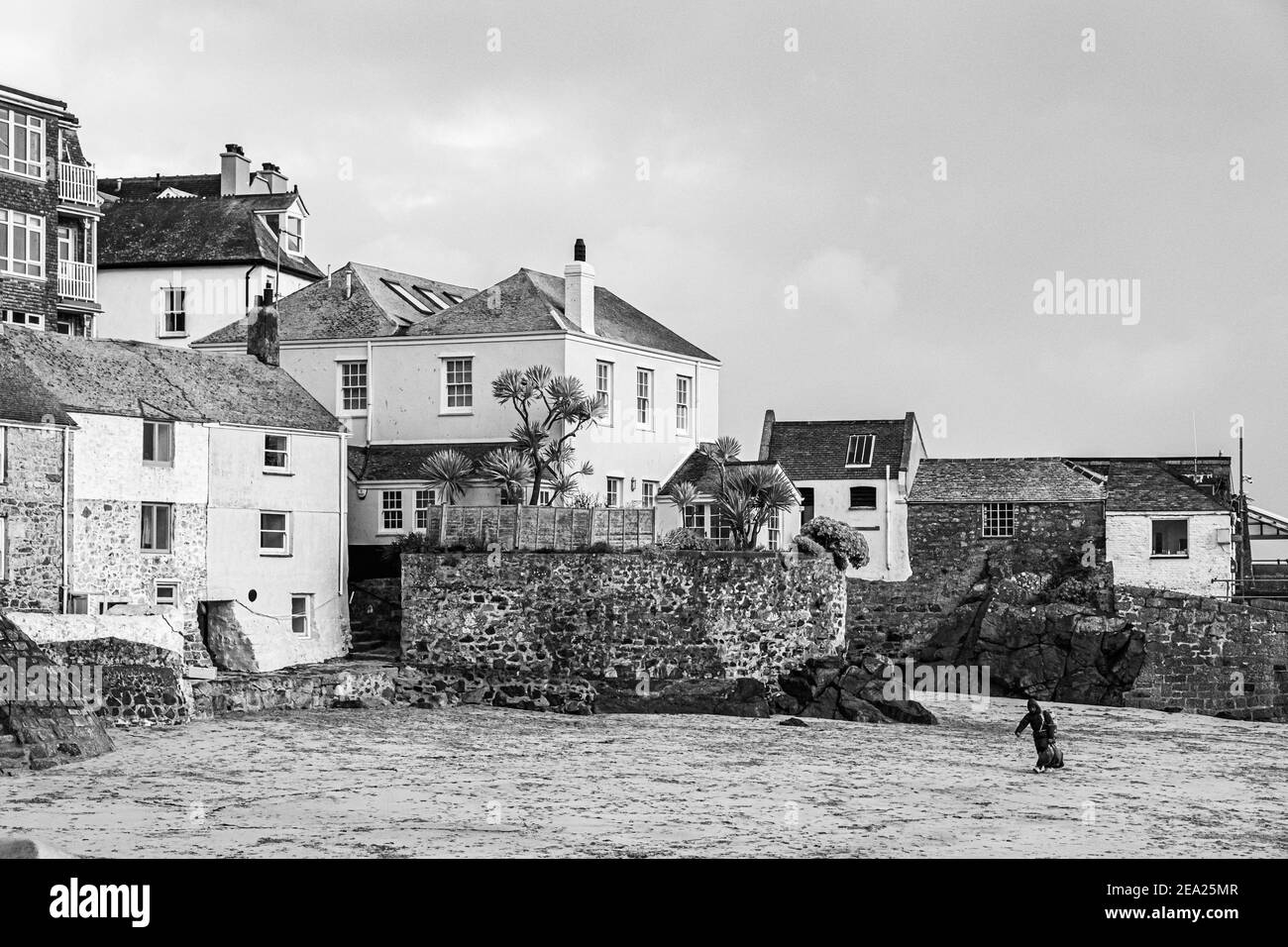 Sole person on the beach carrying a heavy bag towards the harbour wall. No tourists as the global pandemic lockdown has closed all travel and tourism Stock Photo