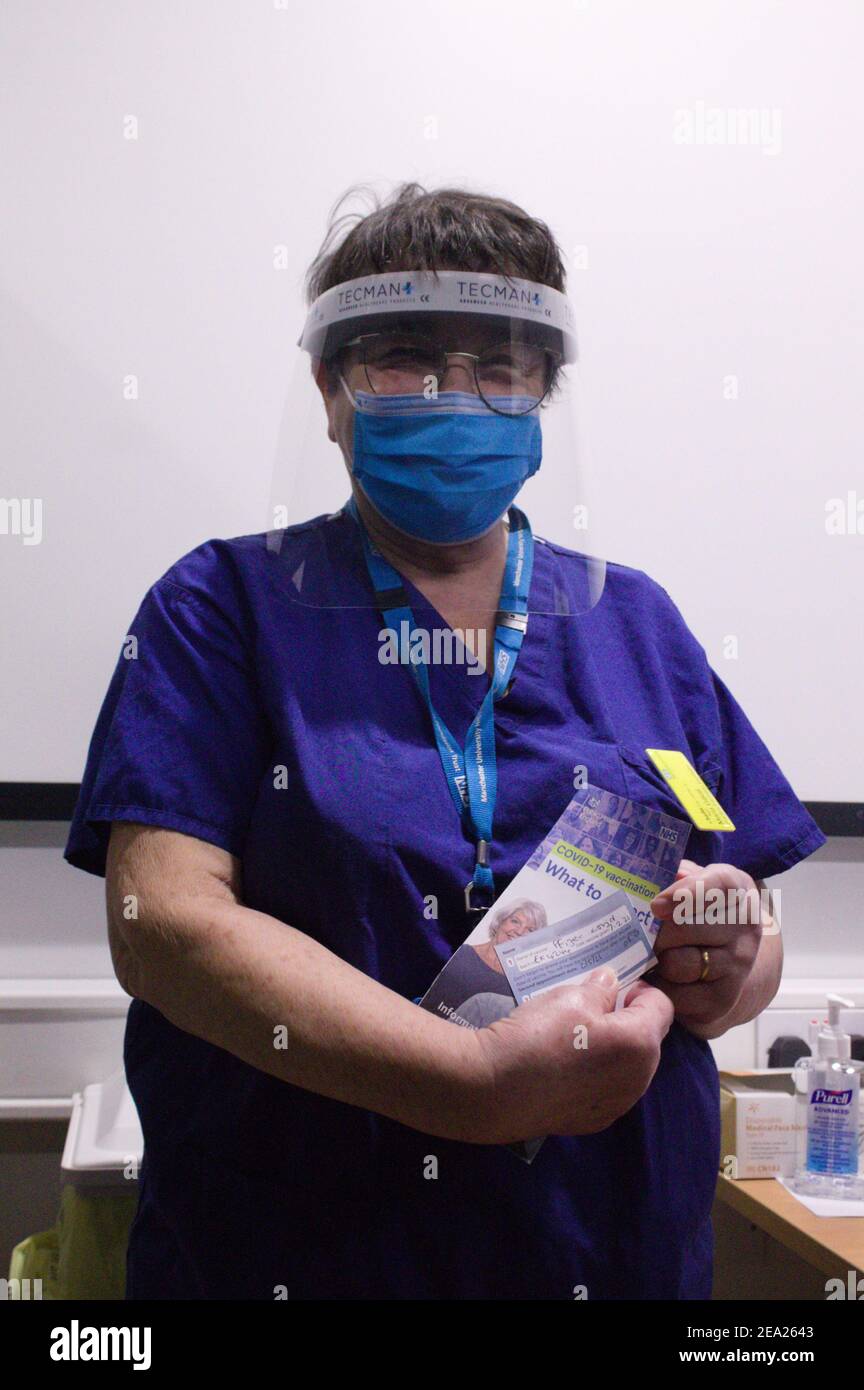 NHS nurse in PPE holding a Covid vaccination card and leaflet. Stock Photo