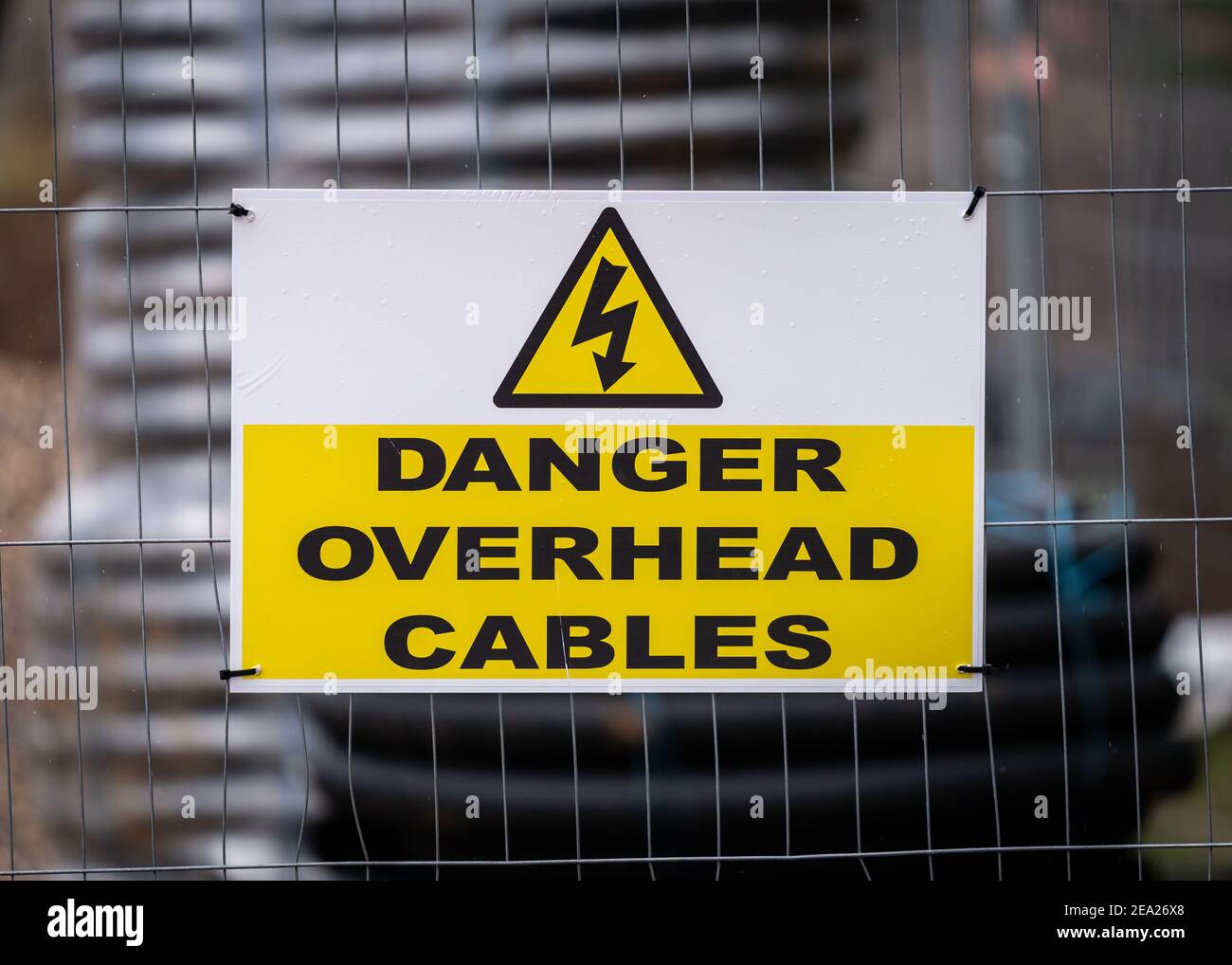 Danger overhead cables modern clean sign in building construction site with yellow electric shock triangle lightening bolt and rolls electrical cable Stock Photo
