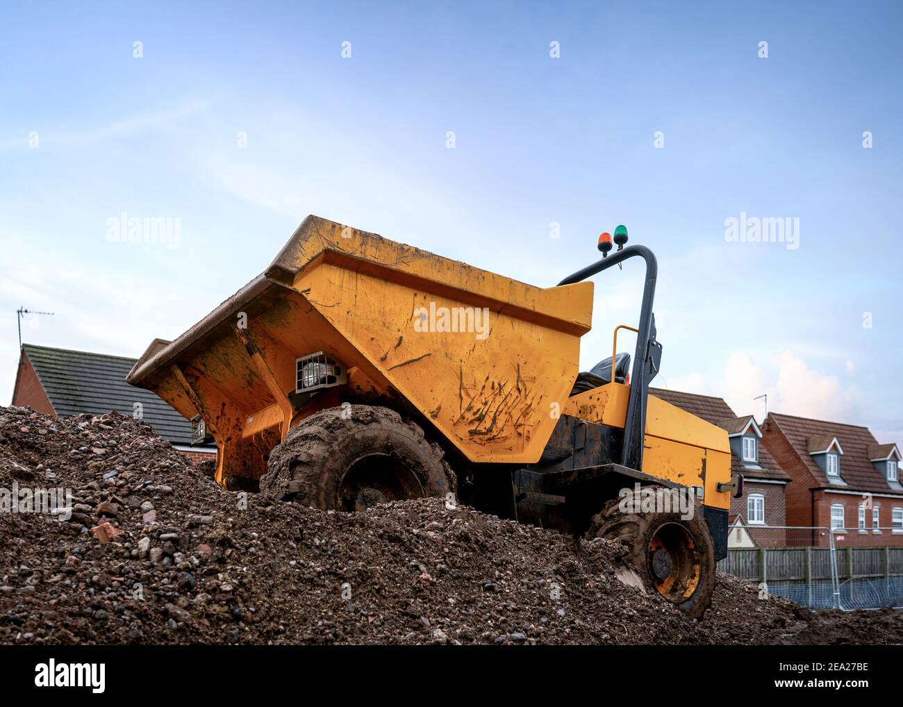 Mini yellow dumper with roll bar and orange flashing lights tipper front bucket  parked on construction mound of soil on new houses industrial site Stock Photo