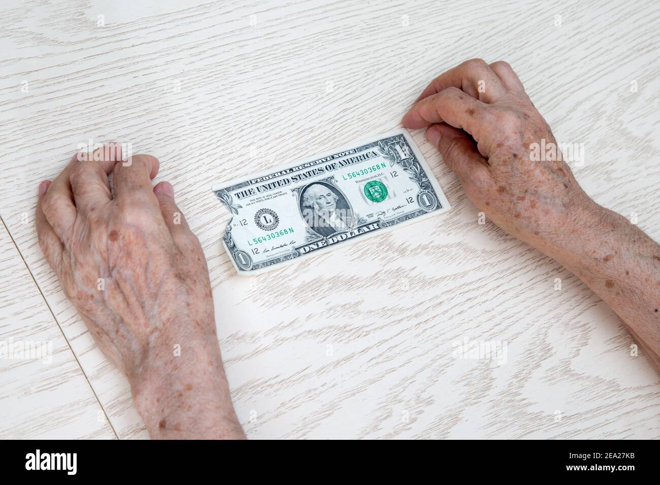 Hands of an elderly woman close-up lie on the table. Between them is 1 old ragged dollar. The concept of despair, poverty, lack of money for basic thi Stock Photo
