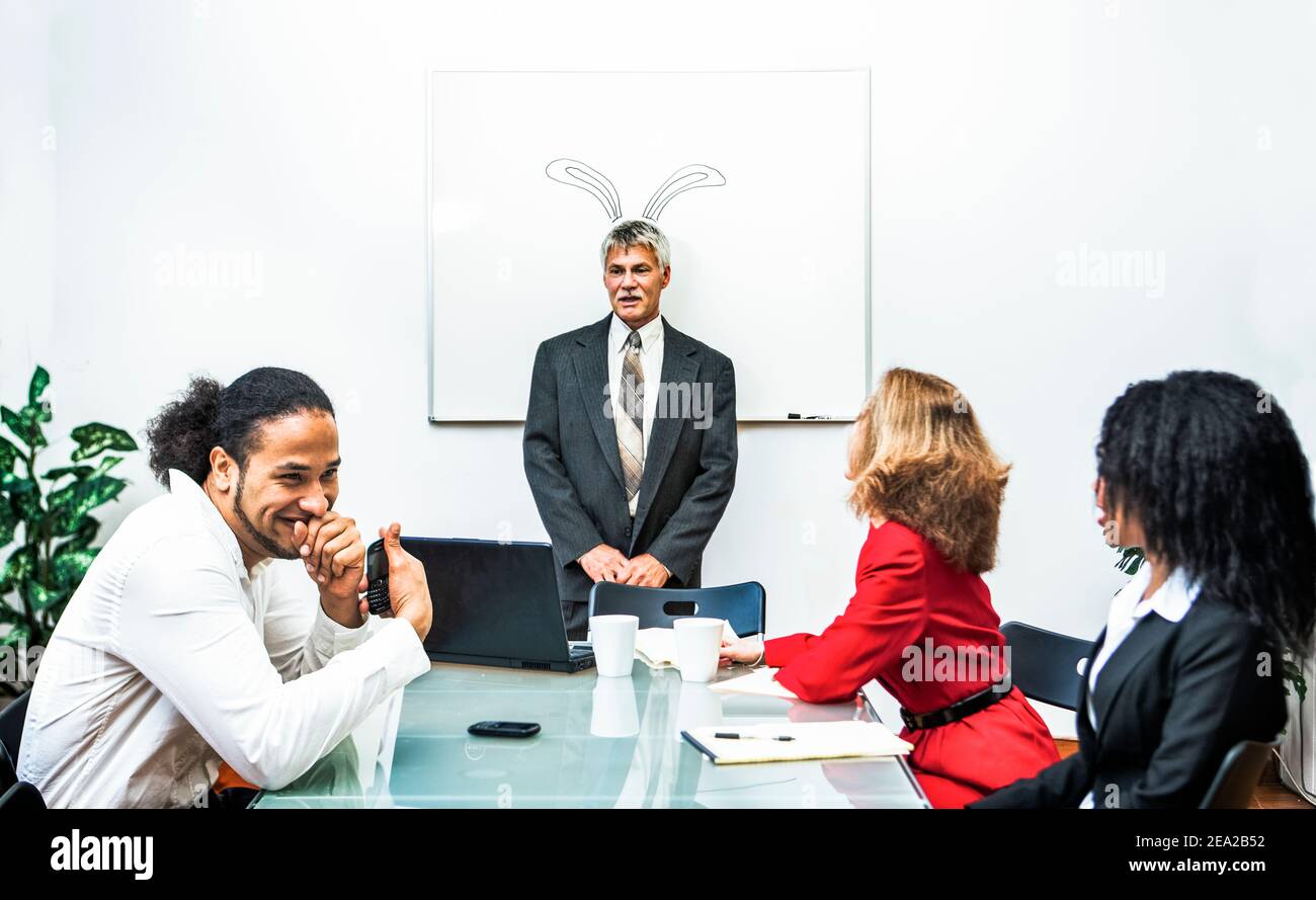 The boss, unbenownst to him, stands in font of a whiteboard with bunny ears drawn on them. Stock Photo