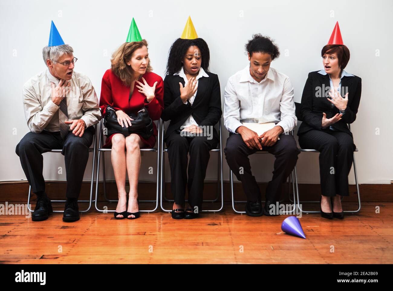 A young businessman drops his party hat while his shocked colleagues look on. Noncomformity concept. Stock Photo