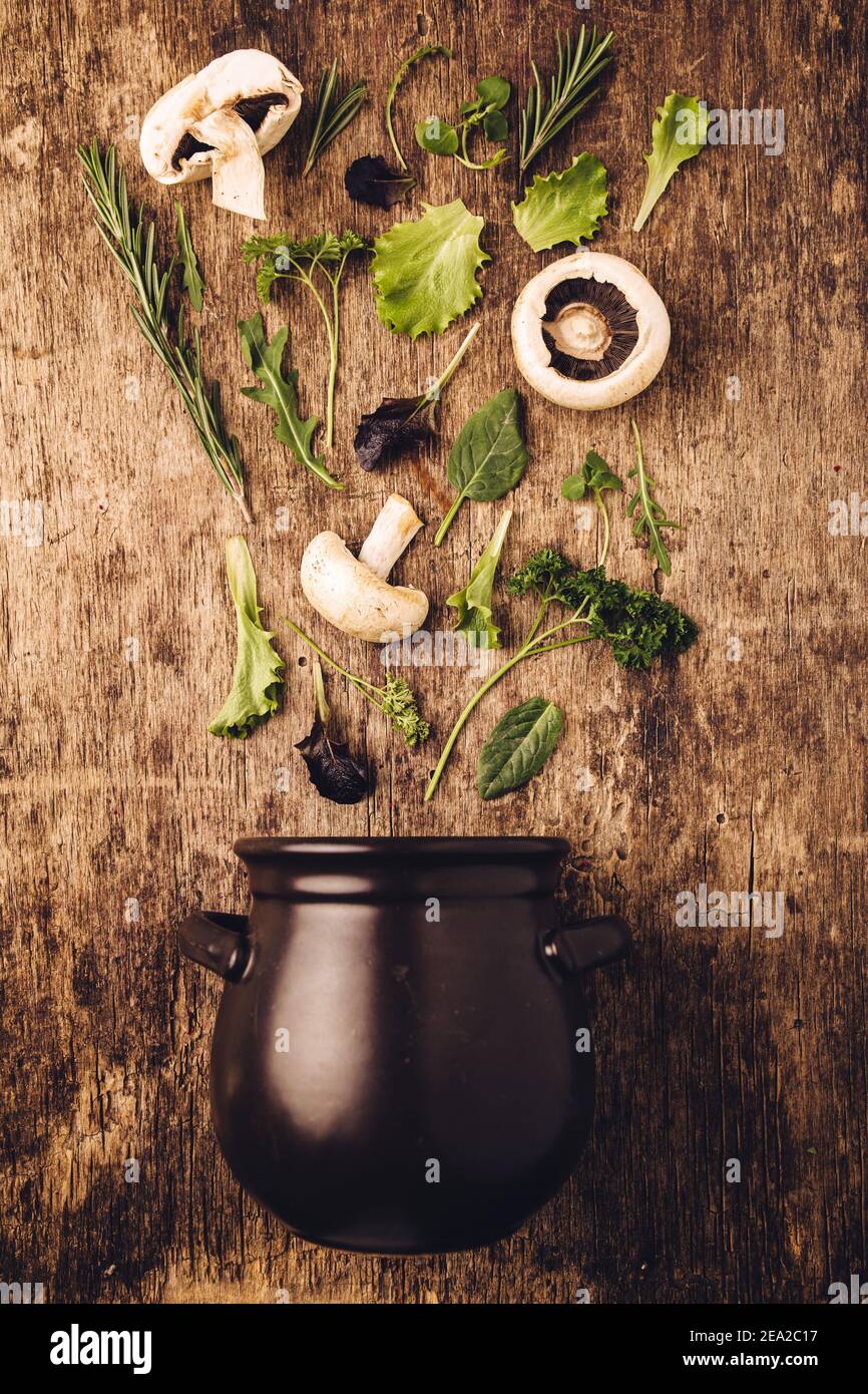 Layout of  fresh vegetables and mushrooms entering in the dark black pot against old wooden kitchen table background with nice, raw, texture. Nature s Stock Photo