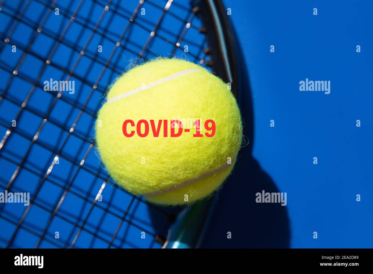 Closeup tennis ball on racket and blue background. Added red text COVID19. Coronavirus