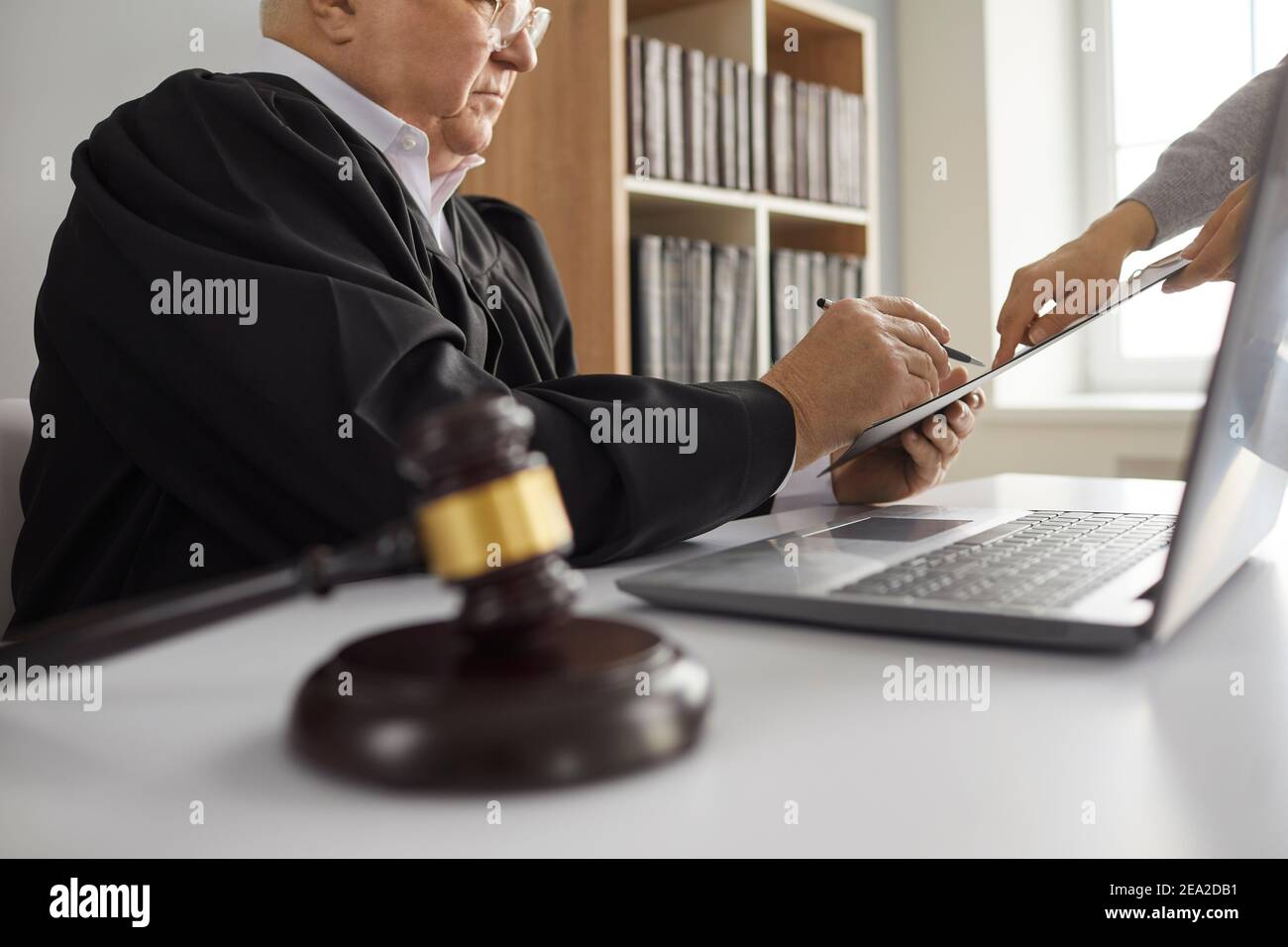 Senior judge sitting at desk at courthouse and signing court order given by lawyer Stock Photo