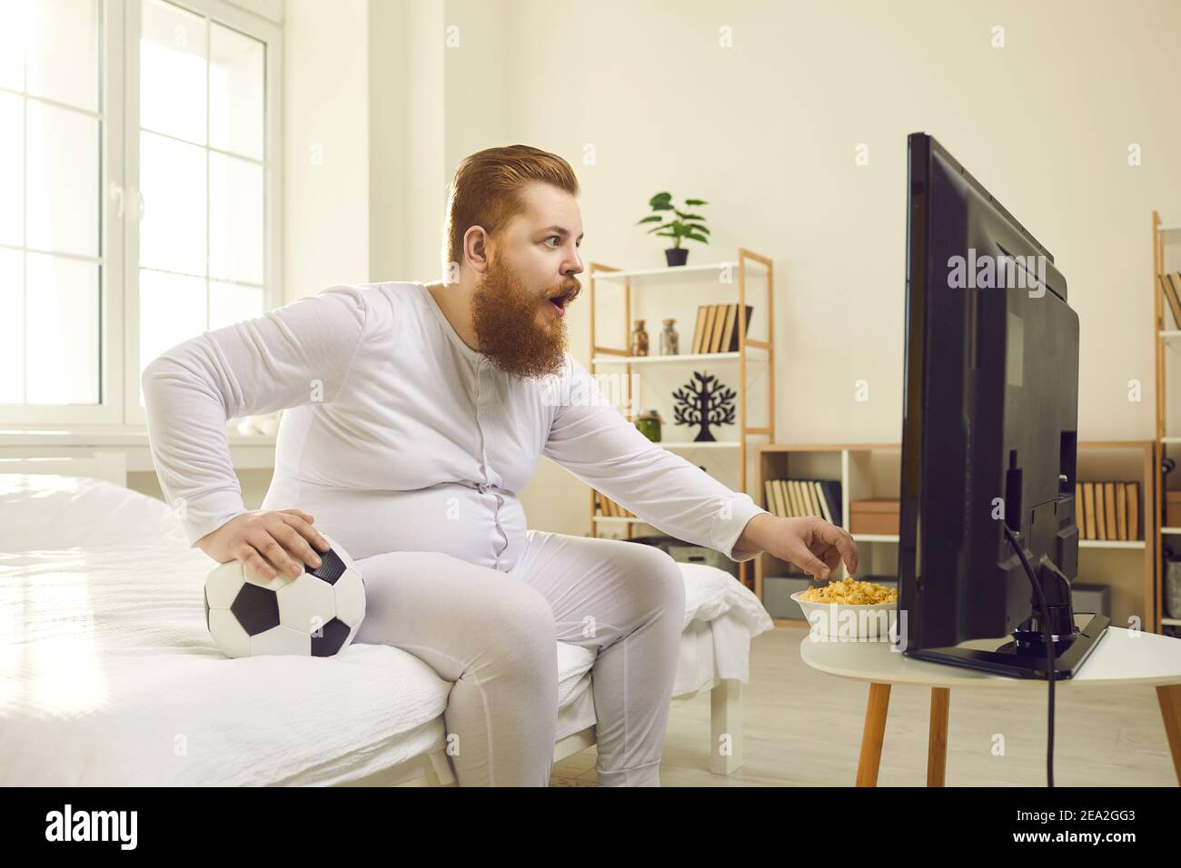 Funny man watching football match on television at home and eating popcorn Stock Photo