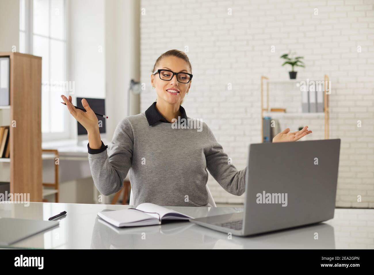 Young positive woman office worker gesticulating during online communication teleconference Stock Photo