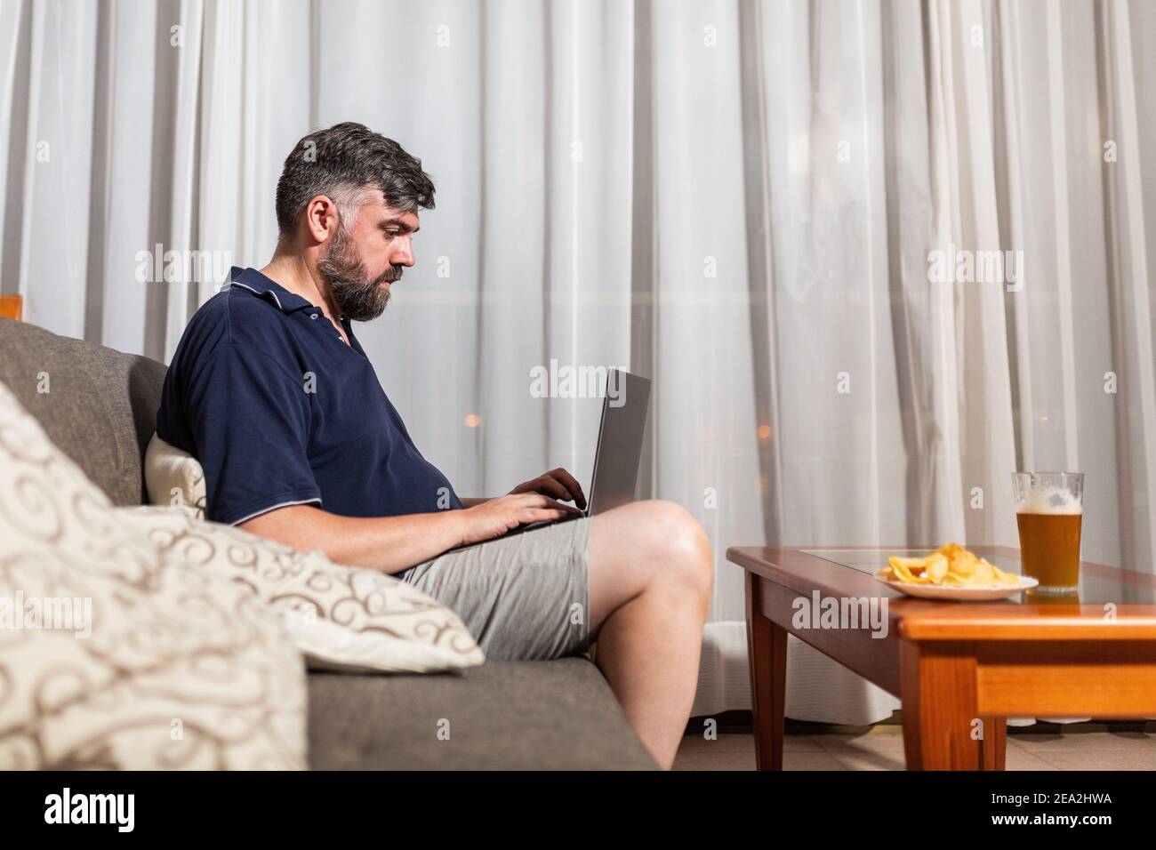 bearded man on sofa uses laptop in dining room overnight Stock Photo