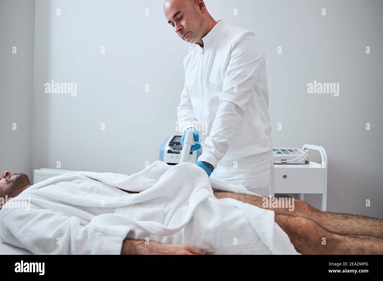 Bald therapist helping man by using BTL machine Stock Photo