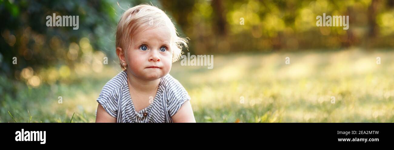Cute baby girl crawling on ground in park outdoor. Adorable child toddler learning to walk. Healthy physical development. Funny kid. Authentic Stock Photo