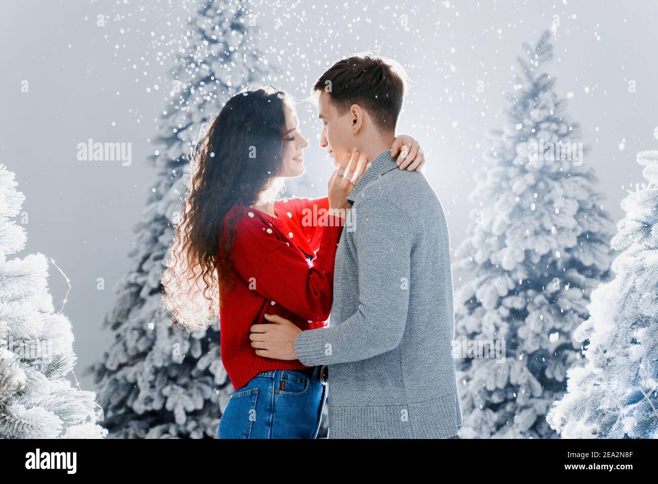 Happy young couple hugs and kiss near christmas trees at the eve ...