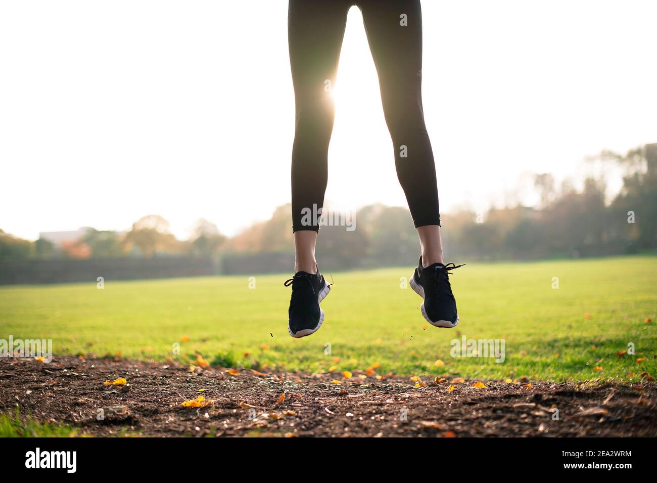 Low angle view of fit, sporty woman jumping in bright green park, close up of legs. Outdoor, active lifestyle concept. London, UK Stock Photo