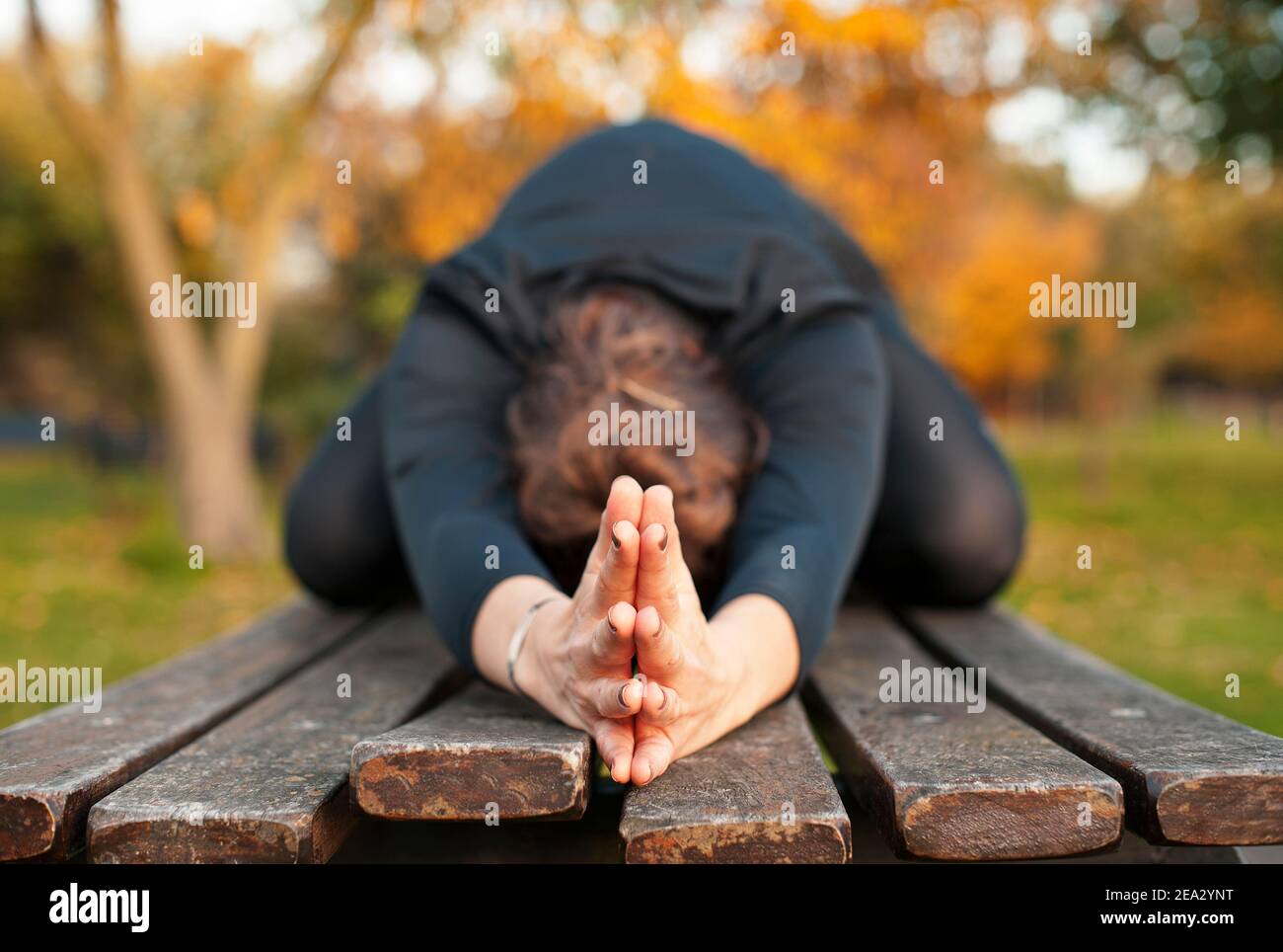 Woman doing yoga stretching outdoor with hands clasped. Focus on hands touching in child pose, Balasana. Workout in nature, healthy lifestyle concept Stock Photo