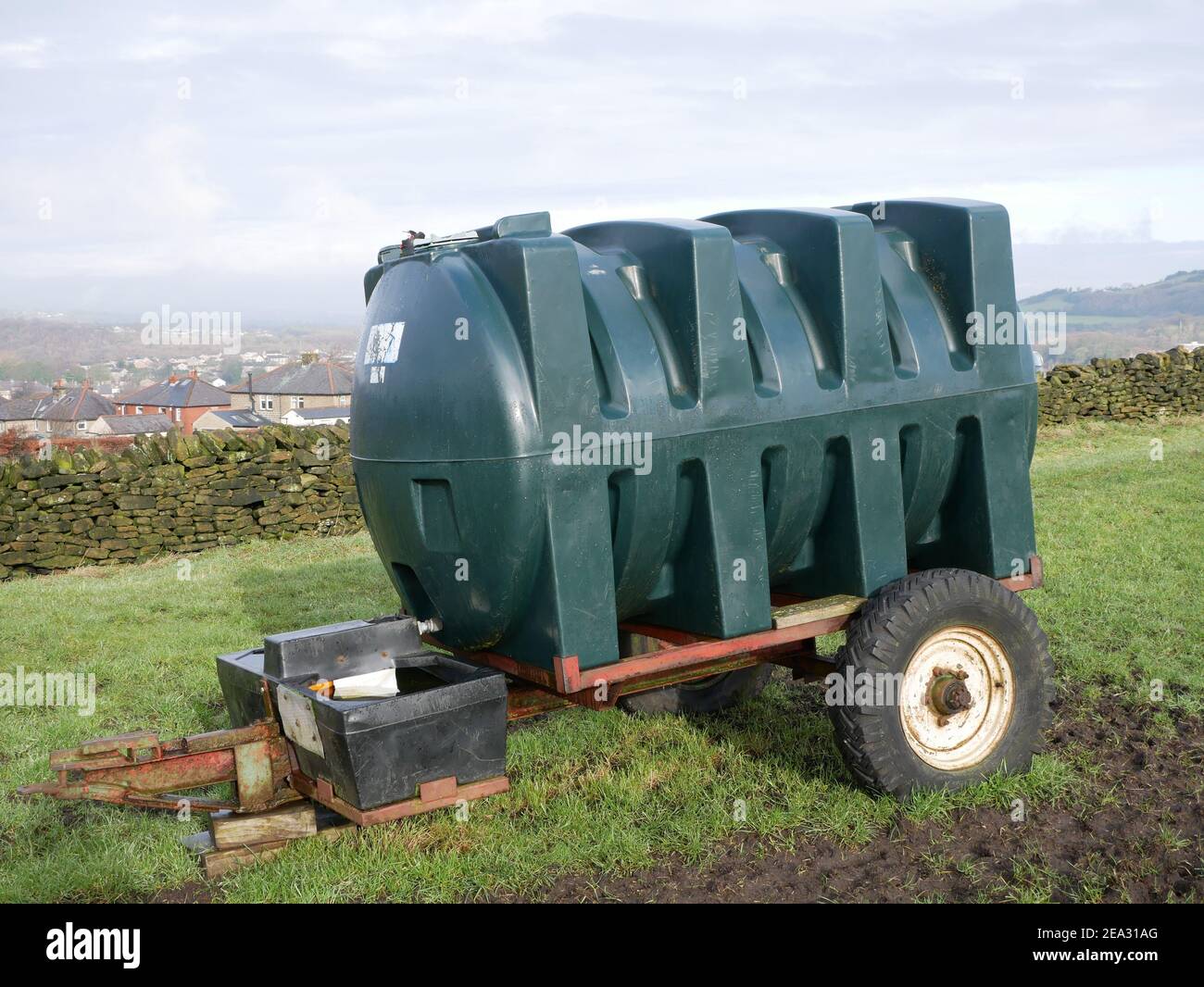 Large green shaped plastic water tank on two wheeled trailer in farm field Stock Photo