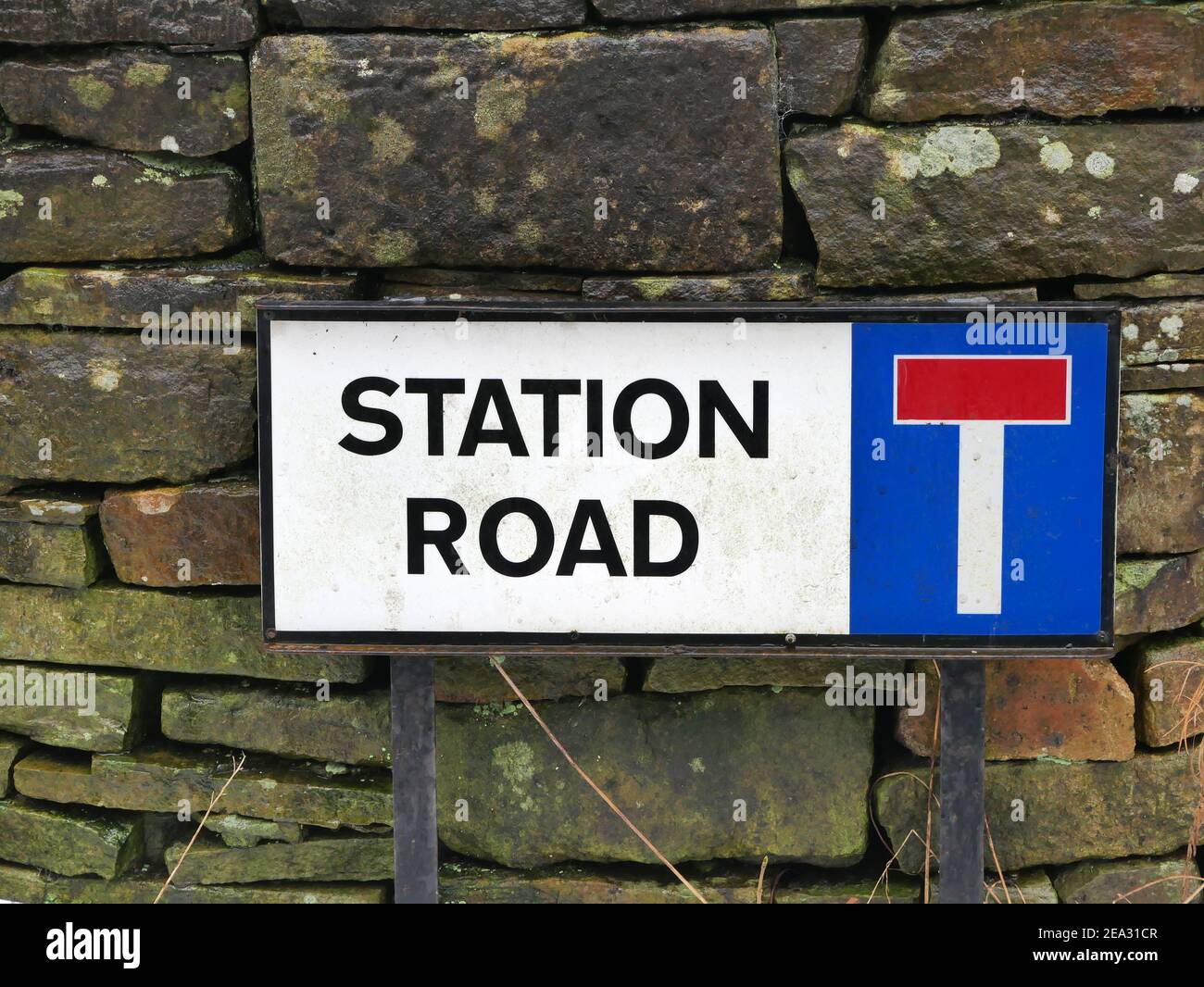 Station road roadside sign black letters and border on white ground red and white letter T on blue square stood against stone wall on metal legs Stock Photo
